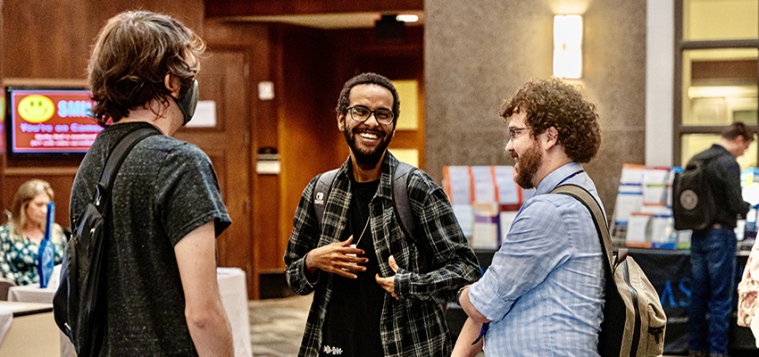 Three students smiling and talking at math conference.