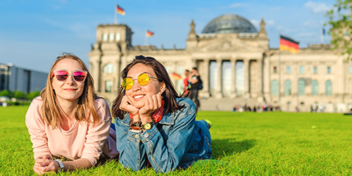 Two female students laying on the lawn in front of a German building.