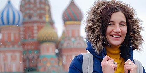 Female in coat in front of Russian building.