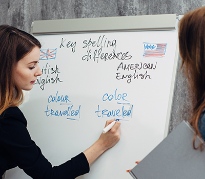 Woman writing on whiteboard while another woman looks on.