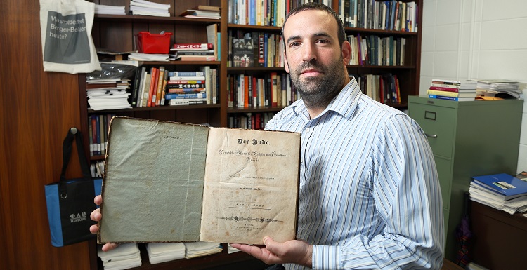 Dr. David Meola, assistant professor of history, holds the journal “Der Jude,” created by Dr. Gabriel Riesser and published in the 1830s to advance Jewish emancipation throughout the German states.