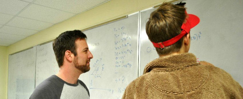 Two students working physics equations at white board.
