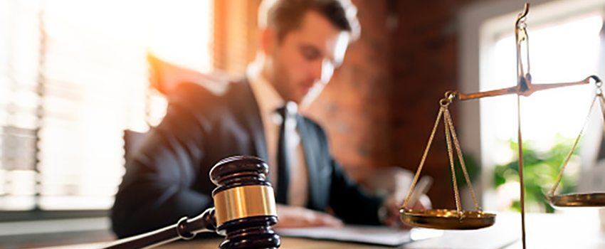 Man at desk with gavel and law scale on desk.