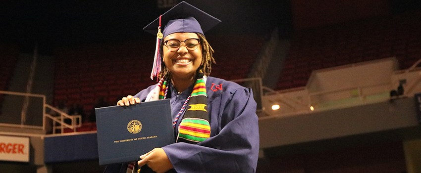 Female student holding diploma at graduation.