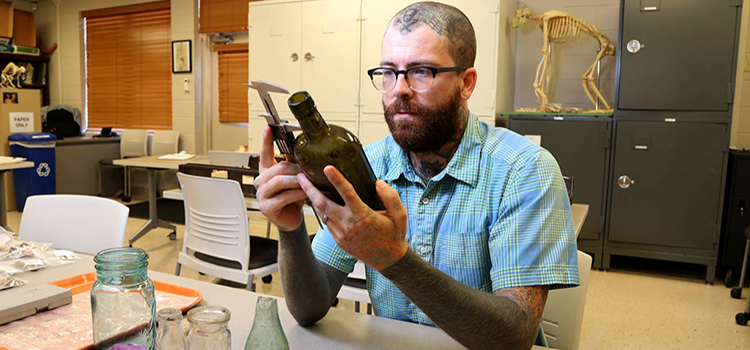 Dusty Norris, a graduate of the University of South Alabama’s anthropology program, is using an archaeology tool to record information about one of the artifacts found at the sites of the shotgun houses in areas of downtown Mobile. This preliminary work is being done as plans for the Mobile River Bridge and Bayway project moves forward.