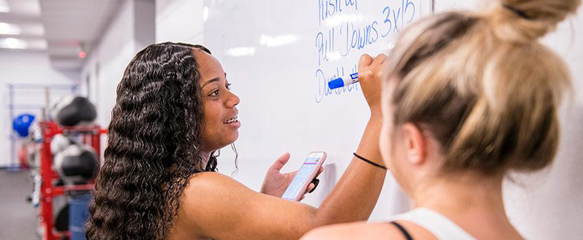 Student writing on white board with another student looking on.