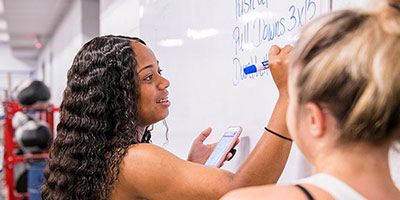 Two students writing workout plan on whiteboard.