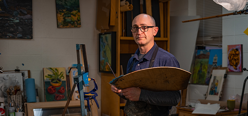 Benjamin Shamback standing in art studio with paint pallet in hands.