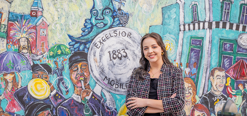 Trinity Walker standing in front of art mural on a wall in downtown Mobile.