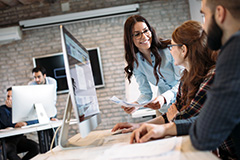 Woman smiling holding papers in front of two people working on a computer.