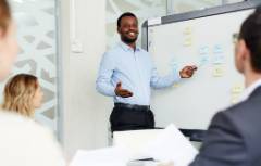 Male pointing to white board talking in front of group.