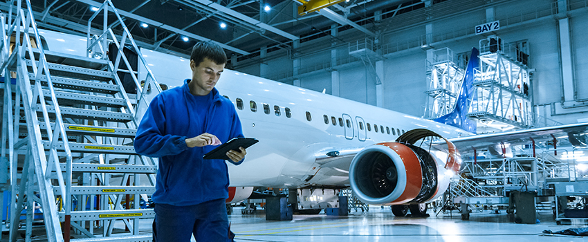 Organizational Leader graduation in airplane hanger taking notes from working on plane.