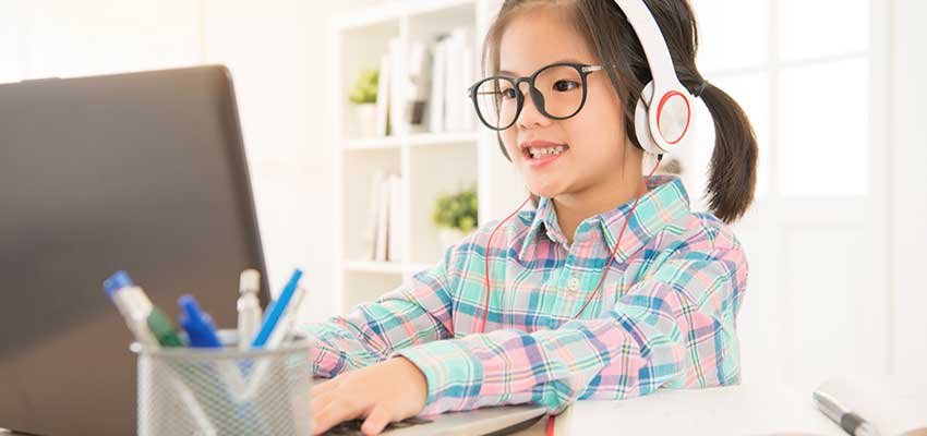 Little girl with headphones on typing on laptop.