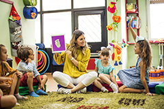 Teacher holding up book while kids sit on carpet in a circle.