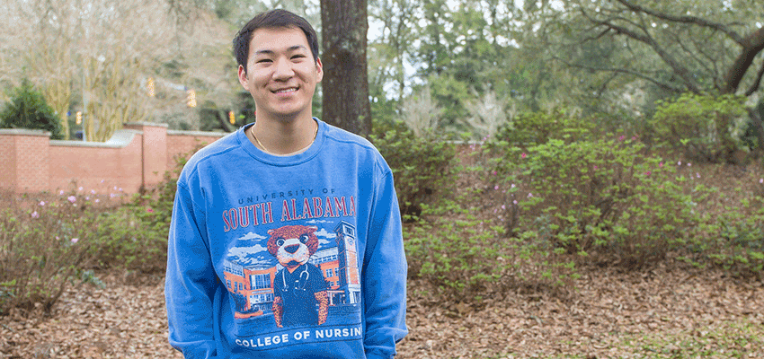 Austin Nguyen in College of Nursing shirt standing outside on campus.