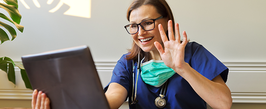 Nurse smiling and waving to computer screen.