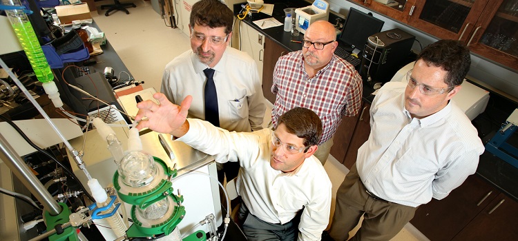 Dr. T. Grant Glover, seated, demonstrates an early-stage prototype of the next-generation carbon dioxide scrubber being developed for the International Space Station. Colleagues Dr. Matthew Reichert, from left, standing, Dr. James Davis and Dr. Kevin West are colleagues on the research project, which is financed by a $1.1 million grant from NASA.