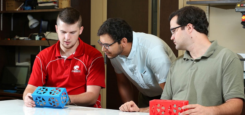 Graduate students Harrison White and Matthew Simmons flank Dr. Carlos Montalvo as they discuss the tradeoff from having two or more miniature satellites, called CubeSats, connected via a tether from an E-Sail. More CubeSats means more tethers and more thrust, but also more chances of tangling.
