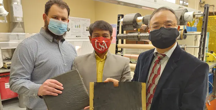 Researchers from the William B. Burnsed Jr. Mechanical, Aerospace, and Biomedical Engineering Department. From L-R; Michael Johnson, MS student and Graduate Research Assistant, Nazim Uddin, MS student and Graduate Research Assistant, Prof. Kuang-Ting Hsiao display a unidirectional ZT-CFRP Prepreg sample produced in Hsiao’s lab and a ZT-CFRP Composite Panel manufactured from stacks of ZT-CFRP prepregs. data-lightbox='featured'