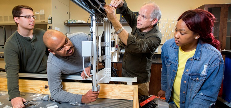 Electrical engineering senior Zack Peavy of Citronelle, mechanical engineering senior Kiante Evers of Gulfport, Miss., and computer engineering senior Ariel Pickett of Montgomery are adjusting the vertical travel distance of the robot head for a space station that will be used to grow crops in space. Assisting the students is Dr. Sam Russ, associate professor of electrical and computer engineering at the University of South Alabama.