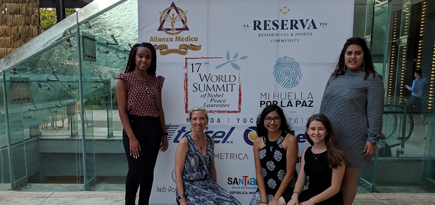 Dr. Cooke with students in front of banner at World summit.