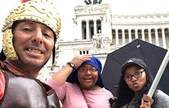 A male with a Roman hat on and two femals with one holding a sword in Rome