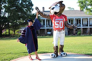 Business student in cap and gown high fiving Southpaw statue on campus.