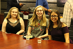 Three female scholars smiling sitting at table