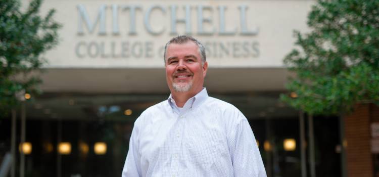 Dr. Chris Lawrey stands proudly outside the Mitchell College of Business.