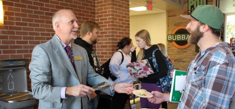 Dean Capella serving king cake to MCOB students in the MCOB lobby.