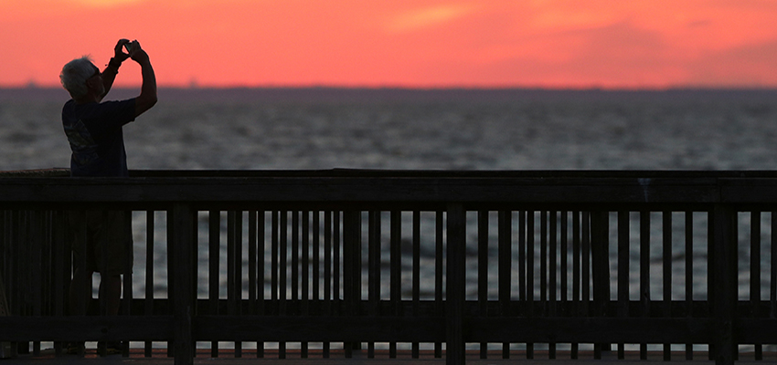 Man taking picture of sunset on pier