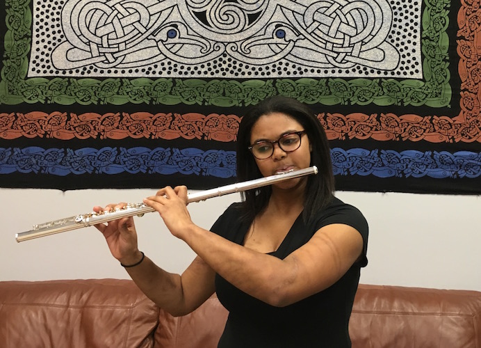 Nicole Carrion playing flute while standing in front of colorful tapestry