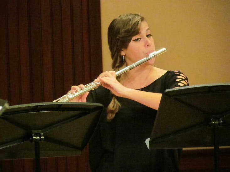 Elizabeth Holmes seated in front of music stand and performing on flute