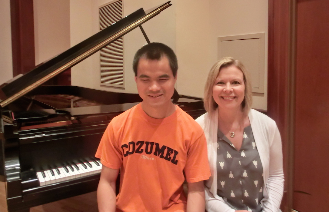Pianists Wei Min Patrick and Tracy Mank seated on piano stool with grand piano in the background