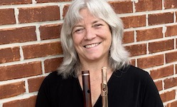 Faculty flutist Dr. Andra Bohnet is pictured posing with her flute next to a brick wall at her home.