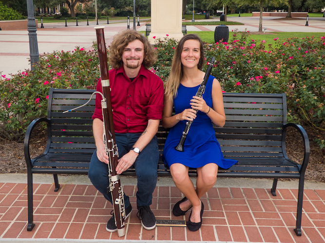 Jake Cannon with bassoon, and Alyssa Weiskopf with clarinet seated on bench in Moulton Plaza