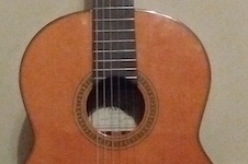 Pictured leaning against a white wall is a concert guitar.