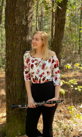 Pictured holding a clarinet while standing in the woods by a pine tree is Cheyenne Higgs. data-lightbox='featured'