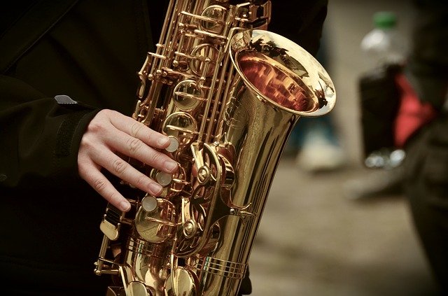 Picture is the bell of a saxophone with performer hands and fingers showing in the picture as well. data-lightbox='featured'
