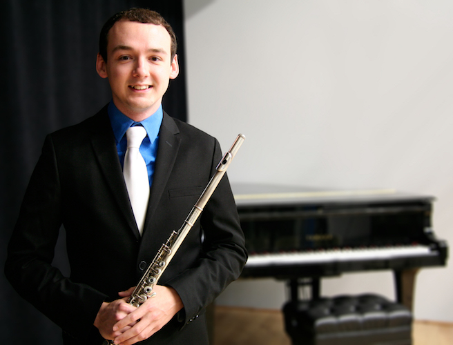 Travis Jones standing with flute in hand and piano in background