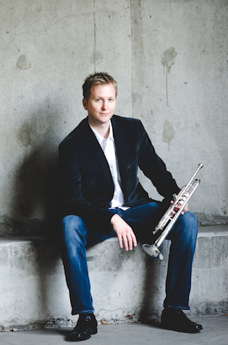 Dr. Randolph Lee with trumpet seated on concrete wall