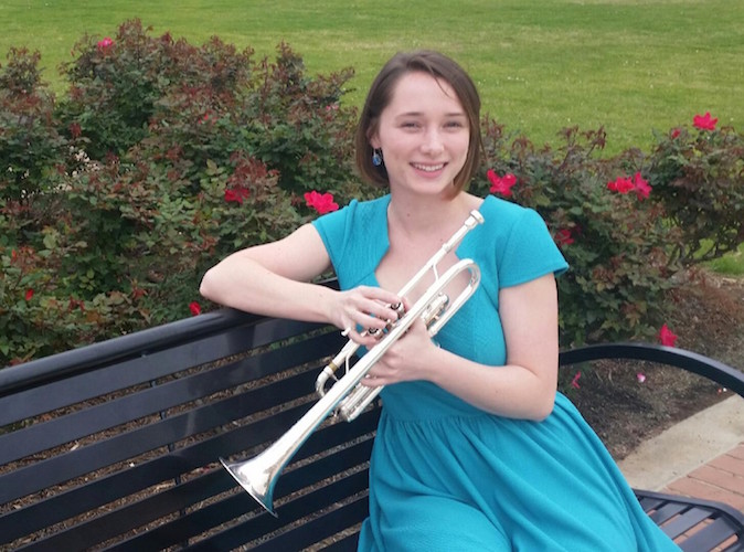 Paige Nelson sitting on park bench with trumpet - roses in background