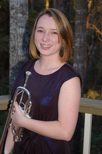 Paige Nelson with her trumpet in night shot with trees in the background