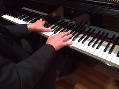 Pictured at the piano keyboard are the hands of the performer only.