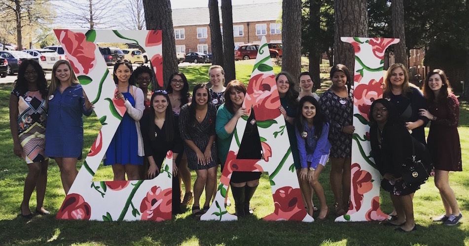 sisters of Sigma Alpha Iota posed among the pine trees with giant floral print Sigma Alpha Iota letters