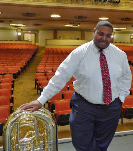 Matthew Selete with tuba standing in auditorium with red seats in the background