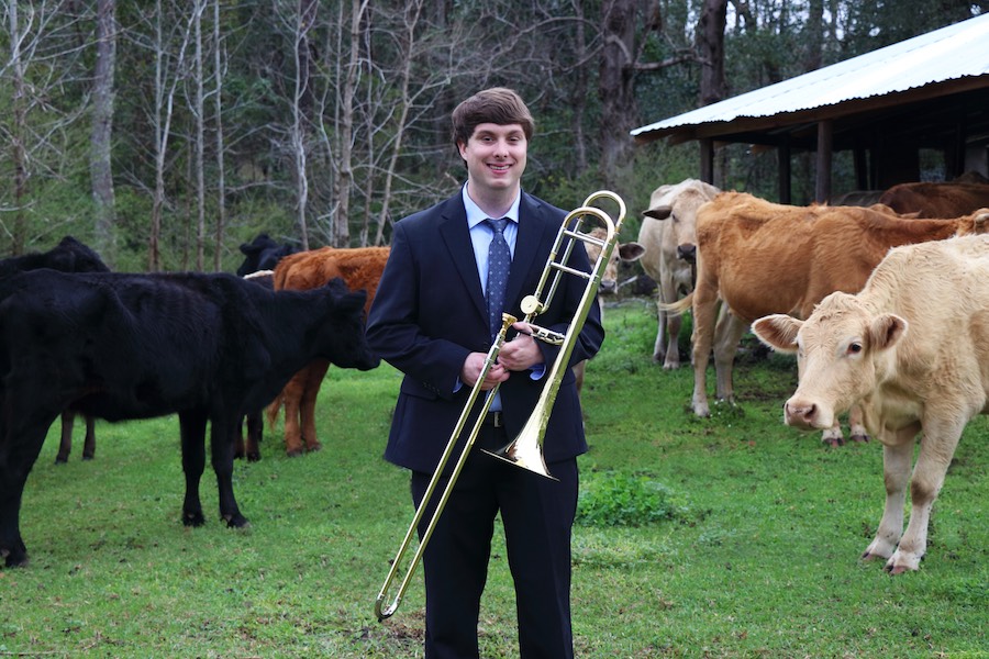 Pictured is trombonist Patrick Whitehurst standing artfully in a corral full of cows. (This is not a mistaken caption!) data-lightbox='featured'