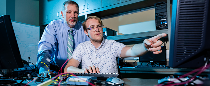 Student pointing to computer with professor behind him.
