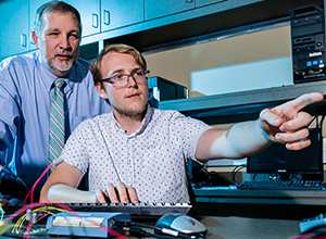 Student pointing to computer with professor behind him,