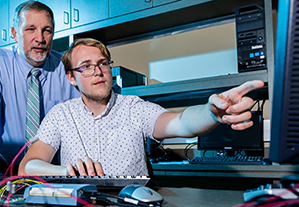 Student pointing to computer with professor behind him.
